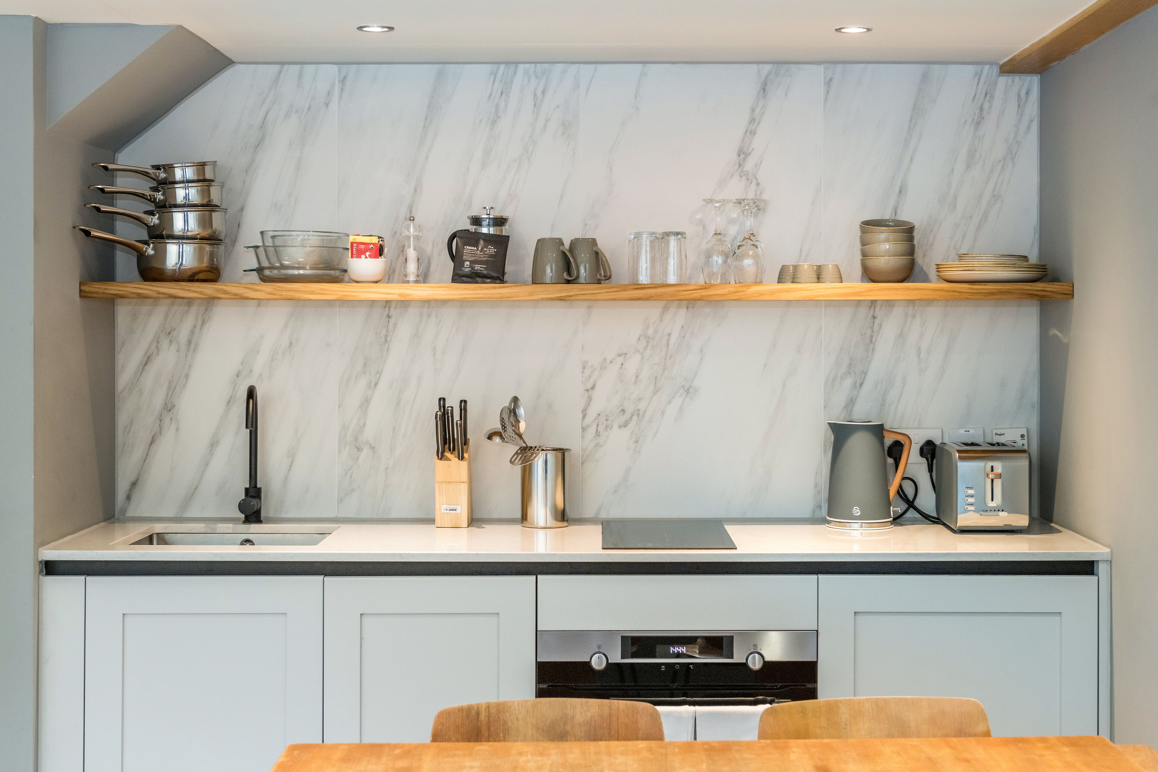 A modern kitchen with marble backsplash, wooden shelves, and stainless steel appliances.