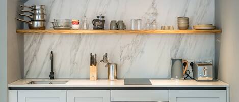 A modern kitchen with marble backsplash, wooden shelves, and stainless steel appliances.