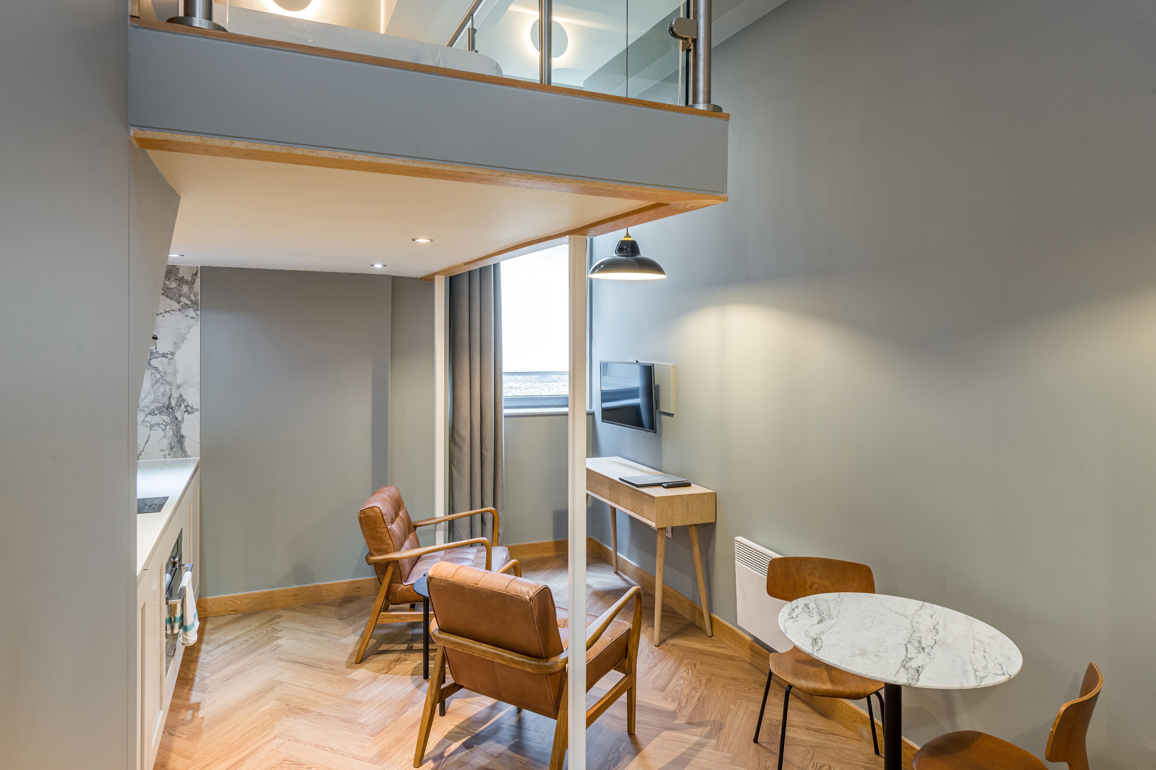 Ein modernes Zimmer mit Schlafgalerie, Holzmöbeln, einem Marmortisch und einem Fernseher.