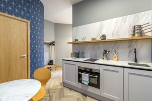A modern kitchen with a marble countertop, built-in oven, and a wooden chair.