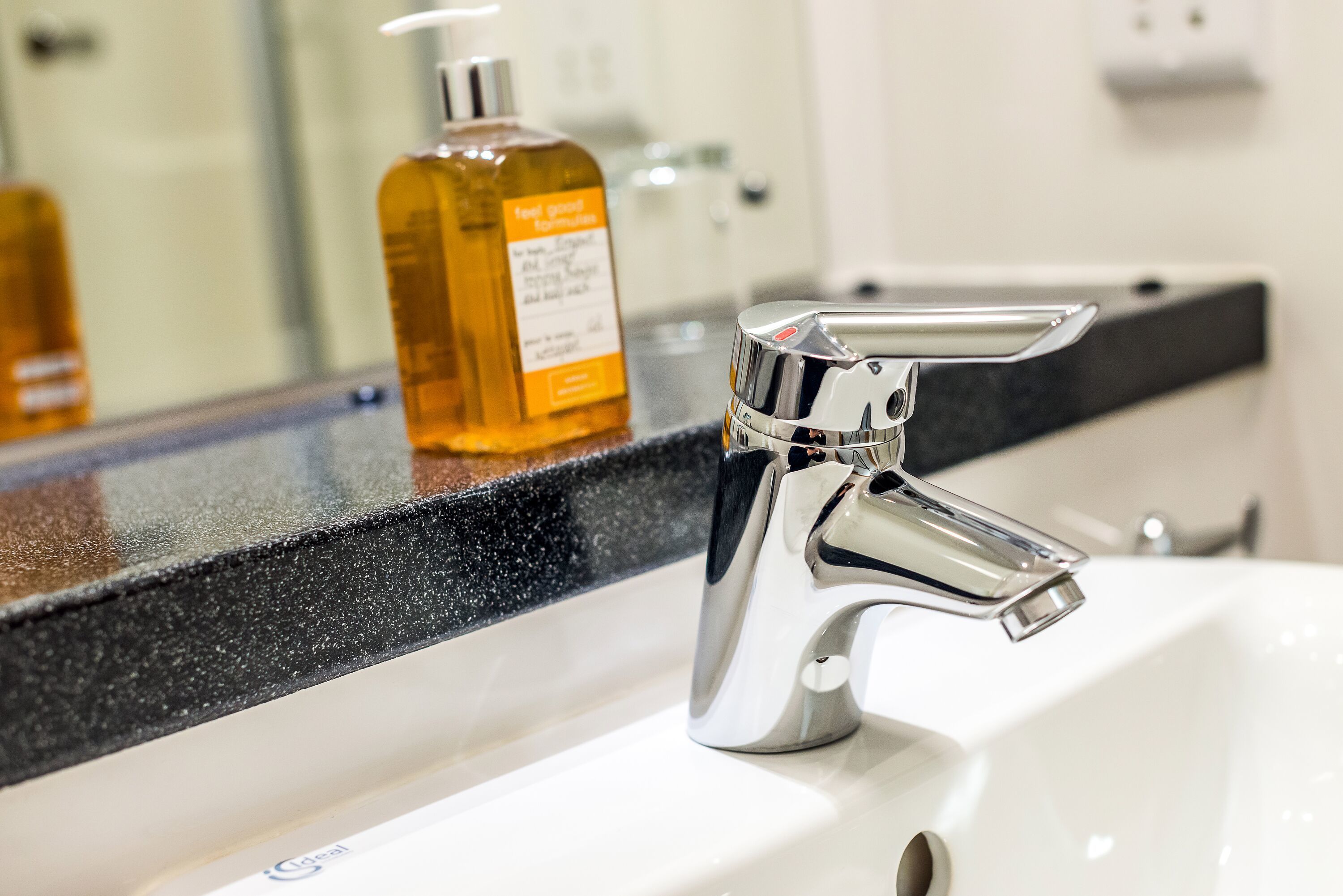 A bathroom sink with a chrome faucet and a bottle of hand soap on the counter.