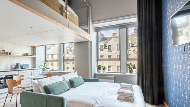 Una habitación de hotel moderna con una cama, un escritorio y vistas a edificios a través de amplios ventanales.