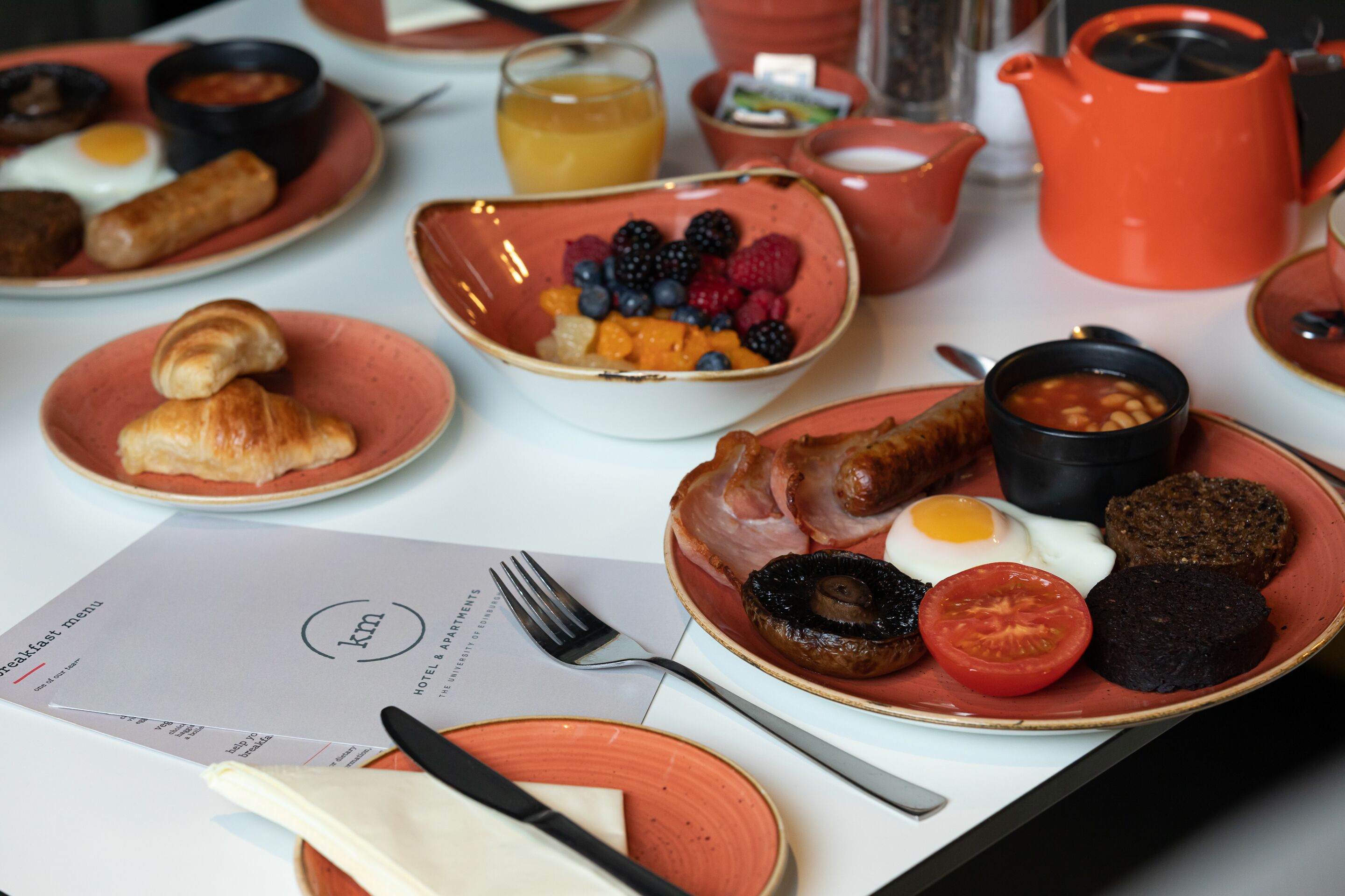 A breakfast setting with plates of food, a menu, and a teapot.