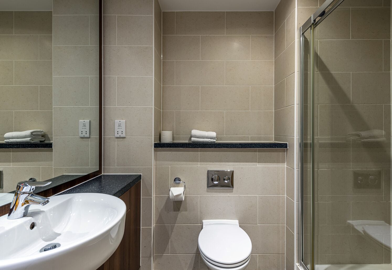 Un baño moderno con un lavamanos blanco, un inodoro y una cabina de ducha de vidrio.