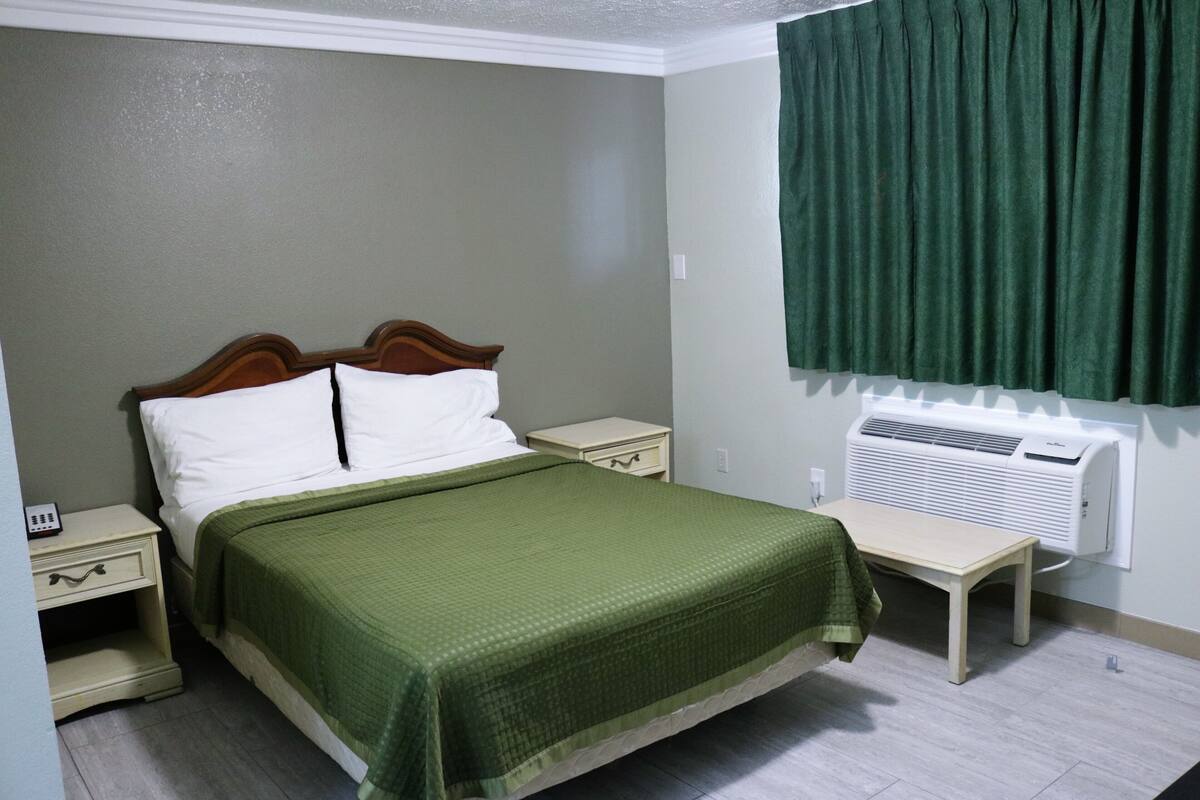 Ein Schlafzimmer mit einem Bett, Nachttischen, einem Heizgerät und einem Fenster mit Vorhängen.