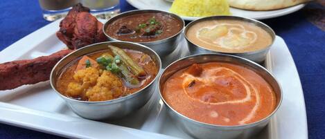 A tray of Indian dishes including curry, rice, and bread, served on a white plate.