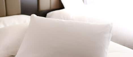 A neatly made bed with white bedding and pillows, a headboard with a light switch, and a window with curtains.