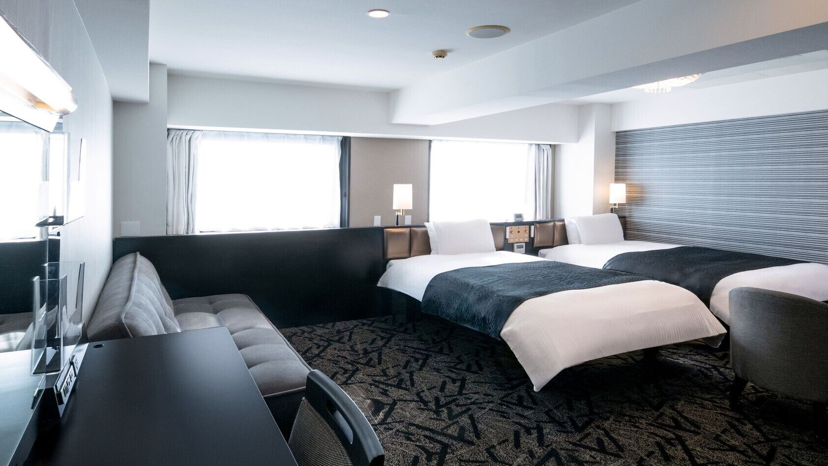 Habitación de hotel con sofá, dos camas, un escritorio y un ventanal grande.