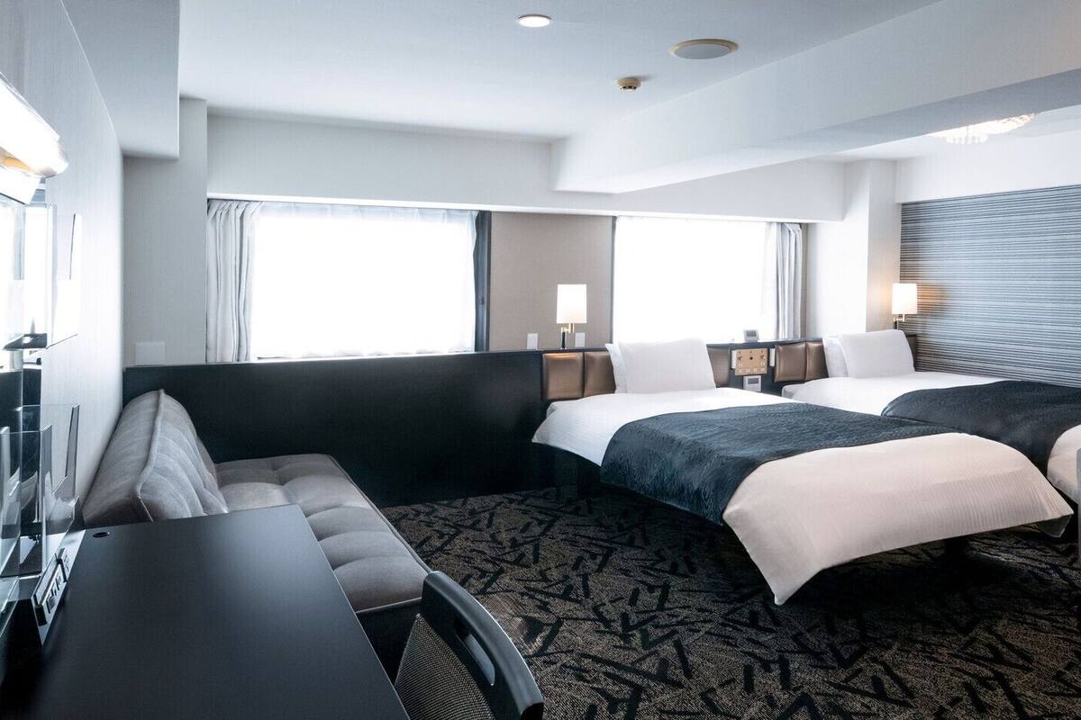 Habitación de hotel con sofá, dos camas, un escritorio y un ventanal grande.