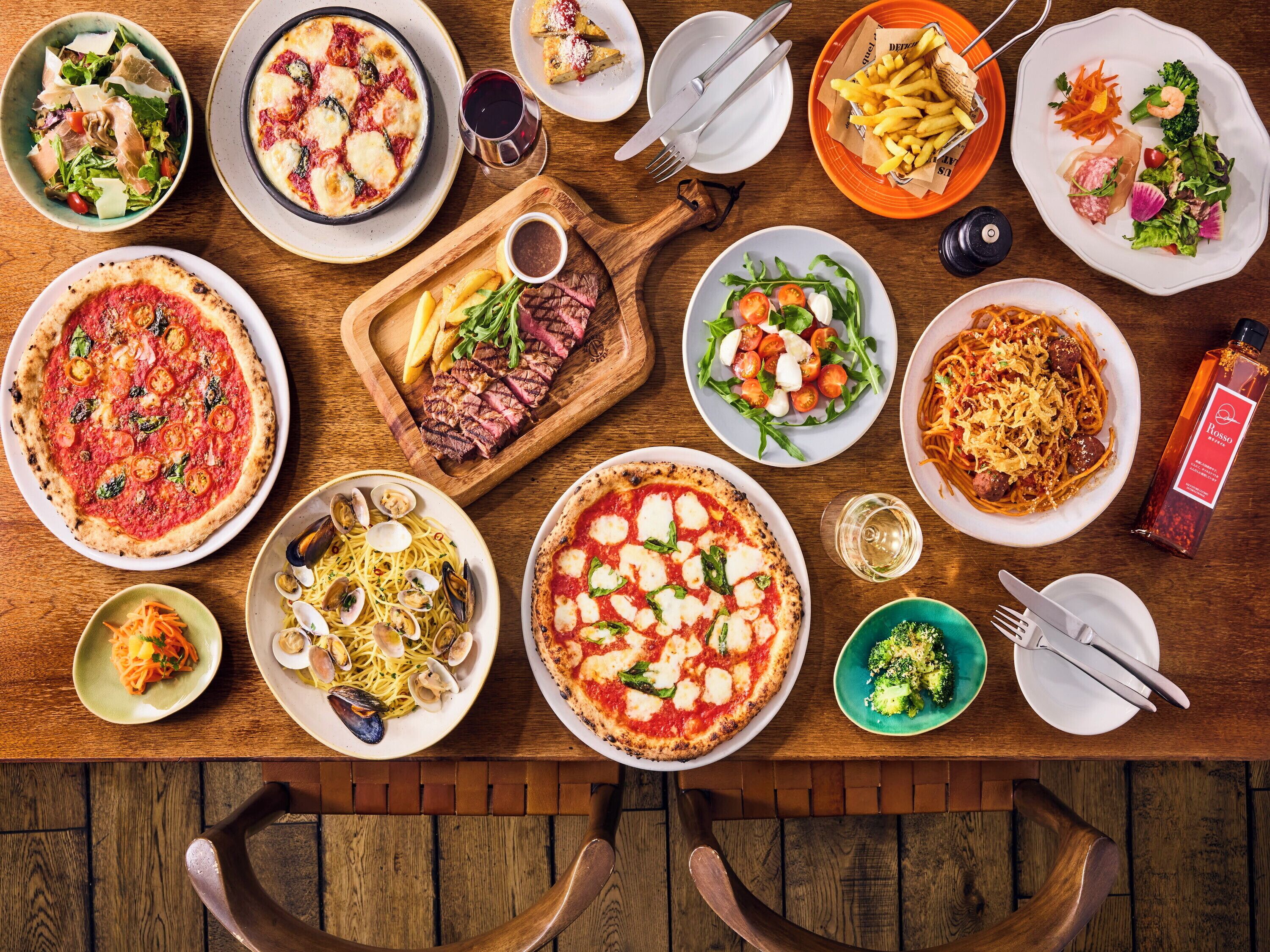 A variety of dishes on a wooden table, including pizza, pasta, and salads.