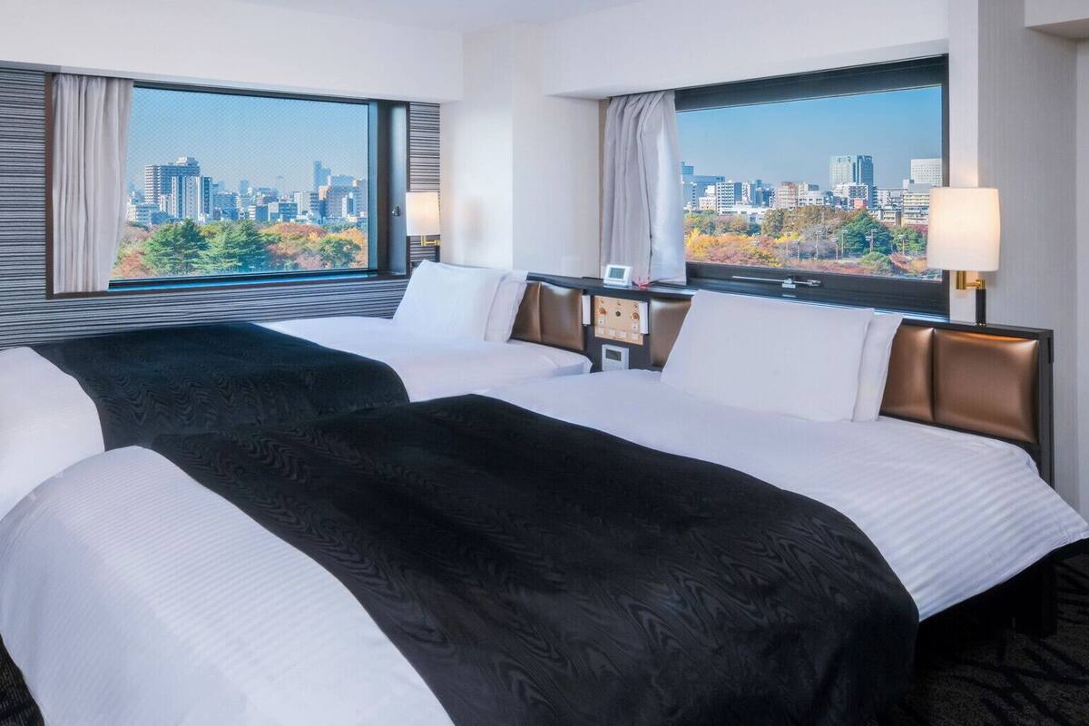 Habitación de hotel con dos camas, vistas a la ciudad, una mesita de noche y una lámpara.