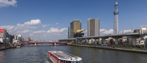 A river with a red and white boat, a bridge, and modern buildings including a tower.