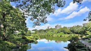 A serene park with a pond, lush greenery, and a distant building. - APA Hotel Tokyo Ojima (Tokyo)