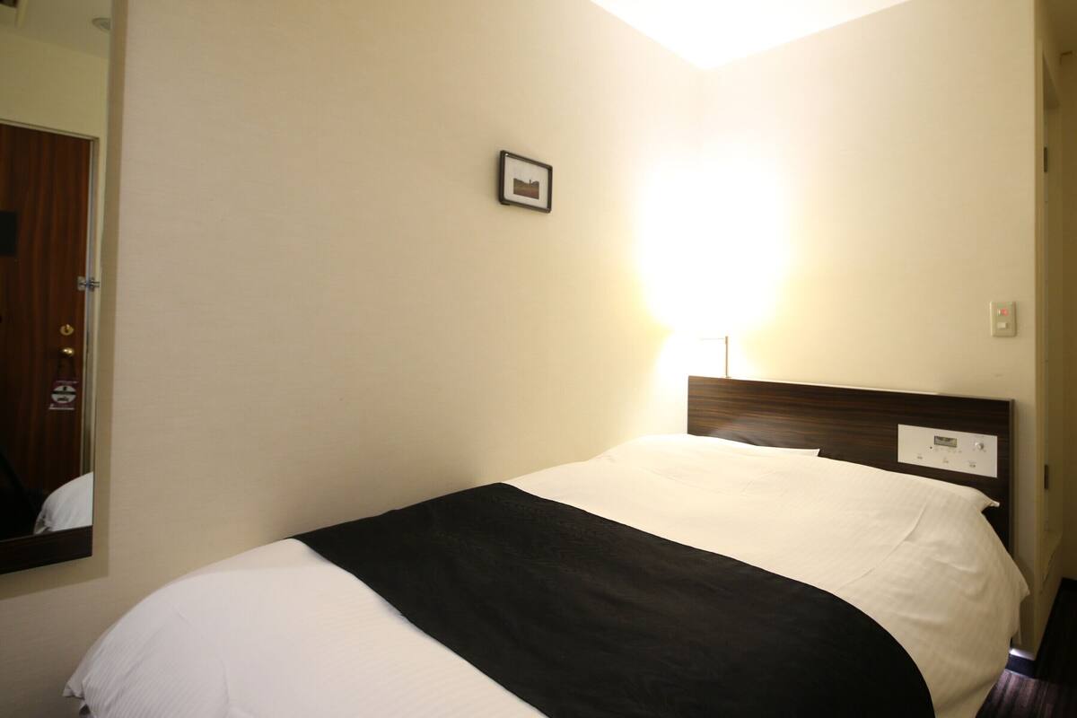 Ein Hotelzimmer mit einem Bett, einem Nachttisch, einer Wandleuchte und einer Tür mit einem Spiegel.