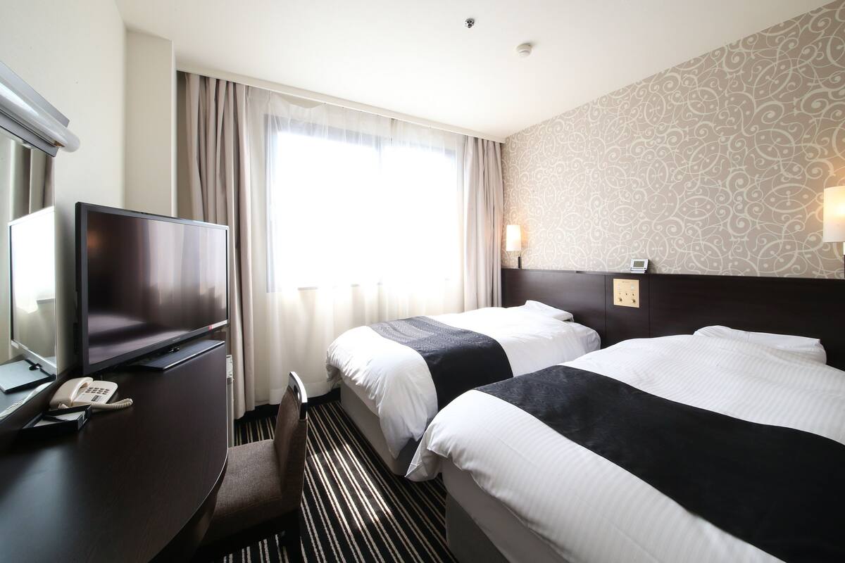 Ein Hotelzimmer mit zwei Betten, einem Schreibtisch mit Telefon, einem Fernseher und einer Wand mit Muster.