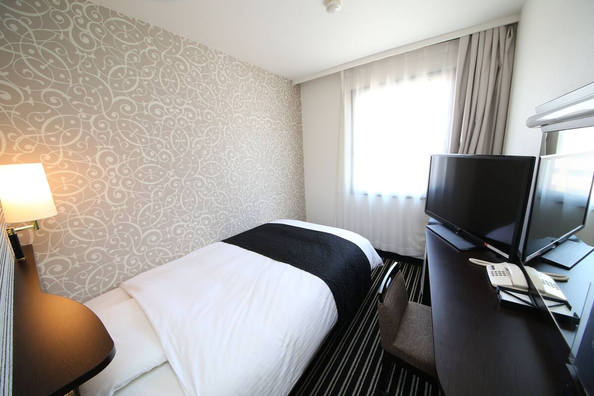 Ein Hotelzimmer mit einem Bett, einem Schreibtisch mit Fernseher, Telefon und Lampe.