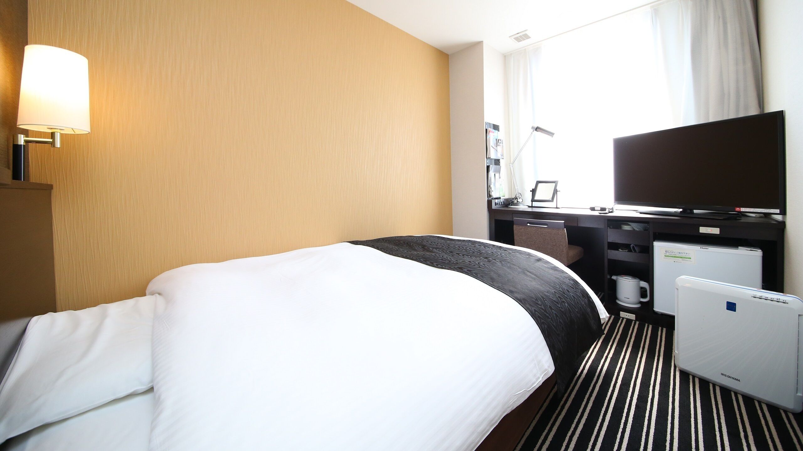 Een hotelkamer met een bed, een bureau, een televisie en een koelkast.