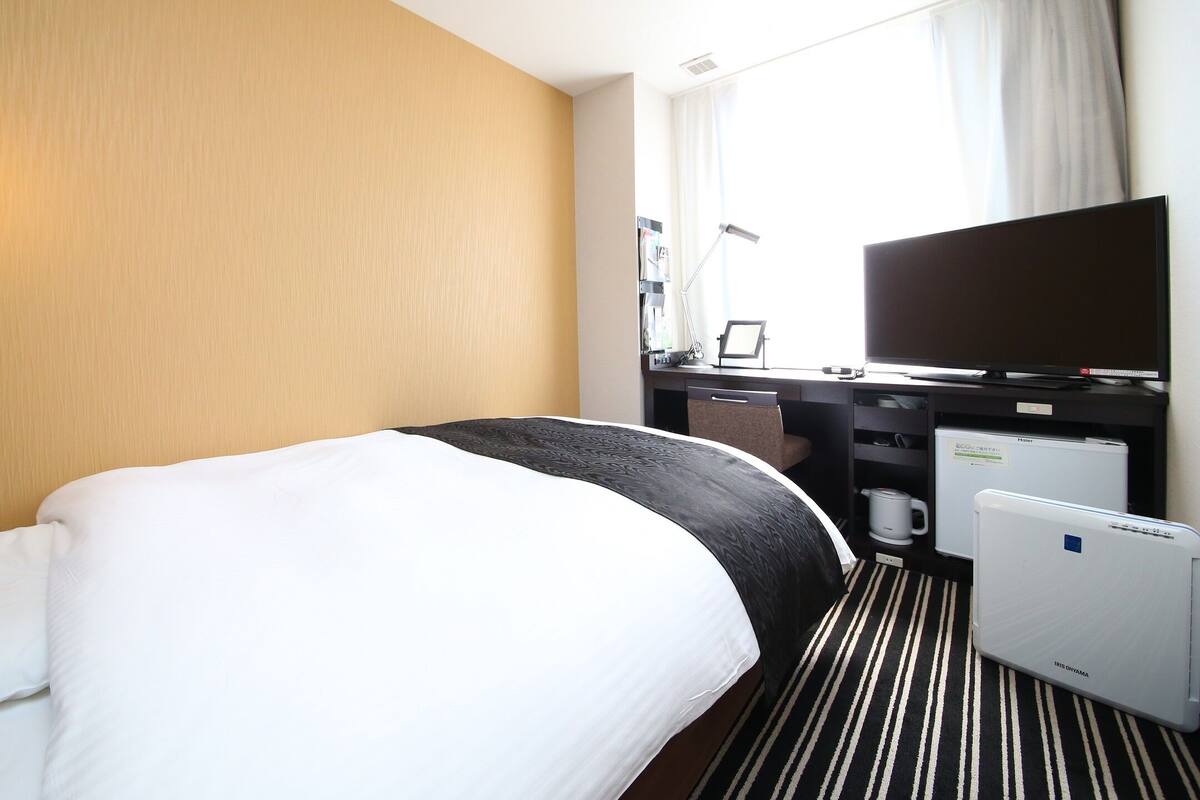 Ein Hotelzimmer mit Bett, Schreibtisch, Fernseher und Kühlschrank.