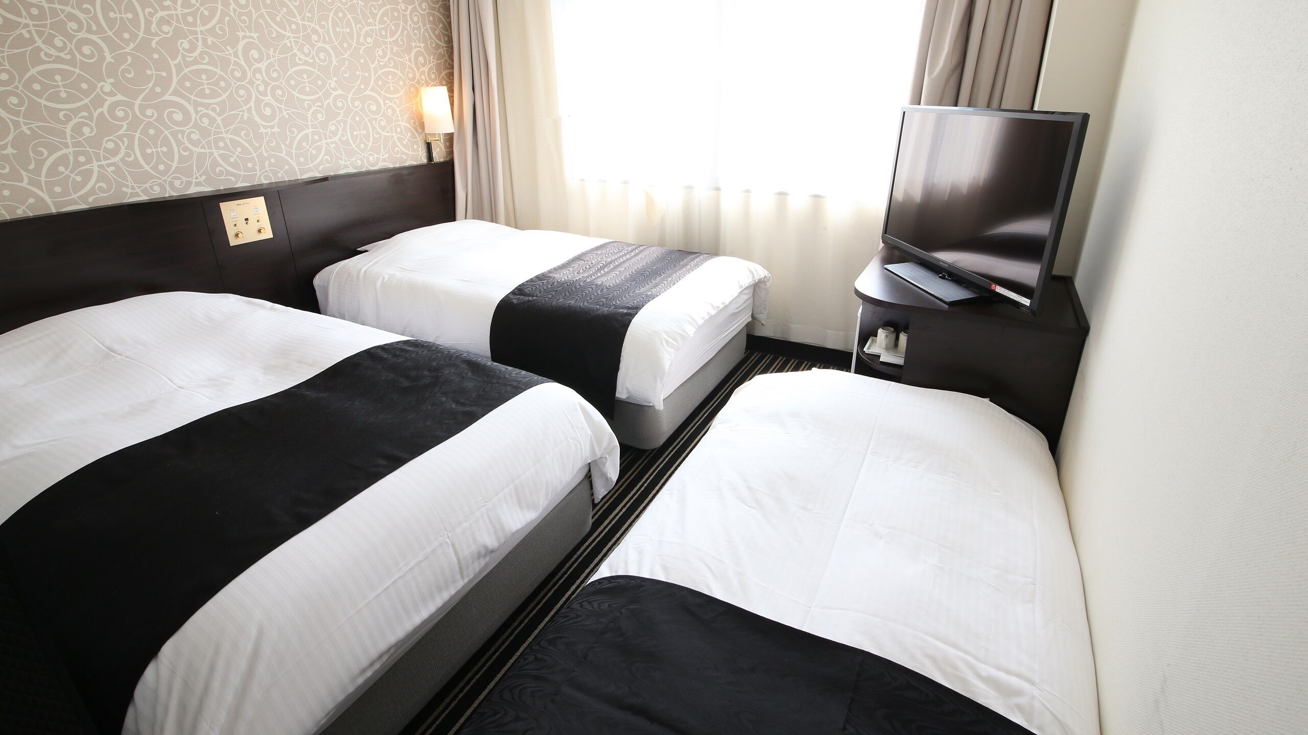 Een hotelkamer met twee bedden, een televisie en een bedieningspaneel aan de muur.