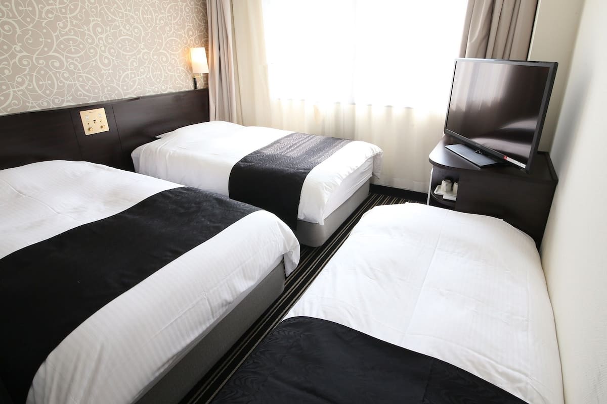 Une chambre d’hôtel avec deux lits, une télévision et un panneau de commande au mur.
