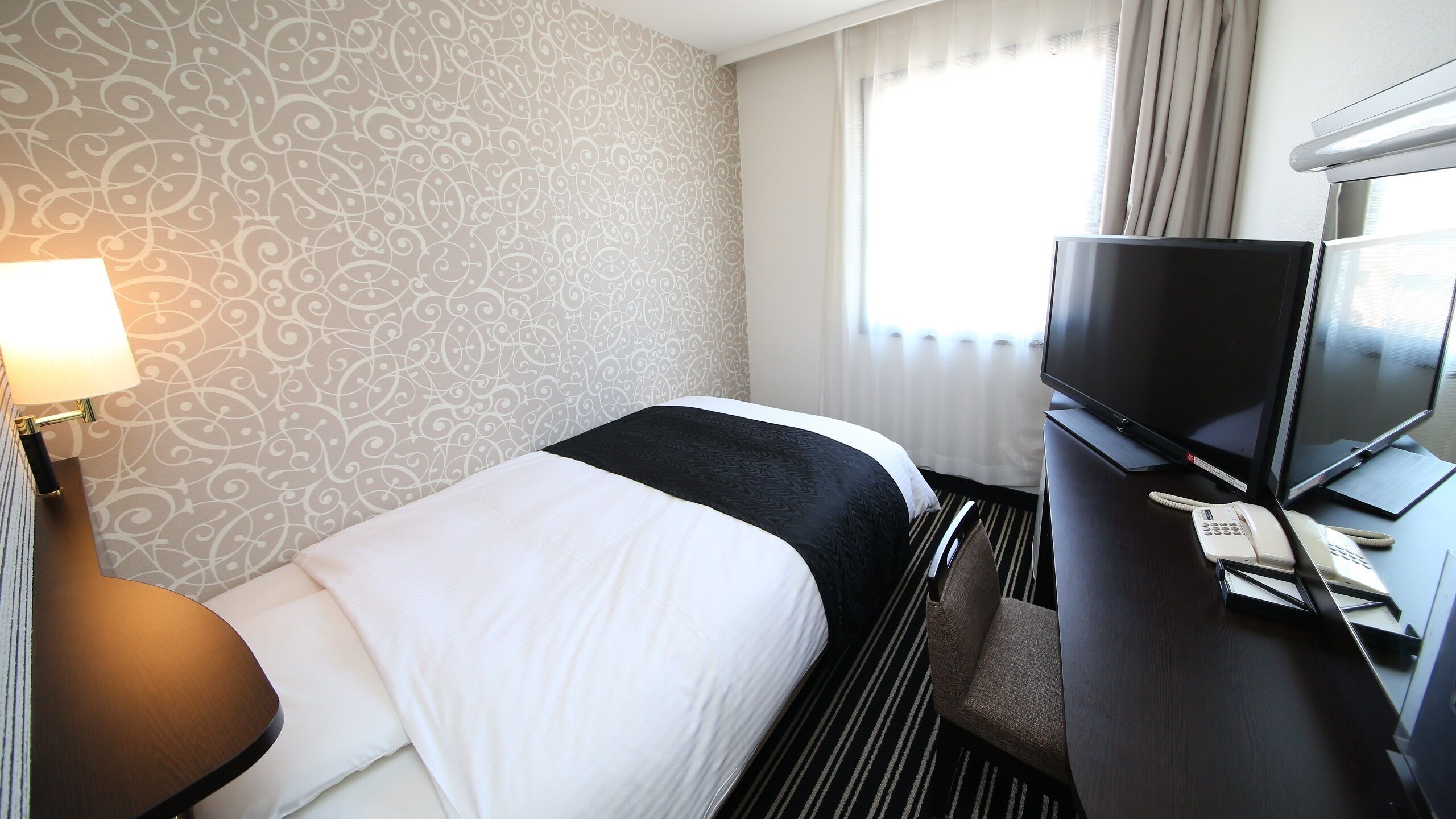 Een hotelkamer met een bed, een bureau met een televisie, een telefoon en een lamp.