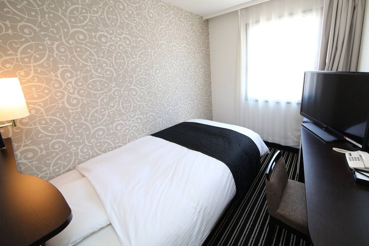 Ein Hotelzimmer mit einem Bett, einem Schreibtisch, einem Fernseher, einem Telefon und einer Lampe.