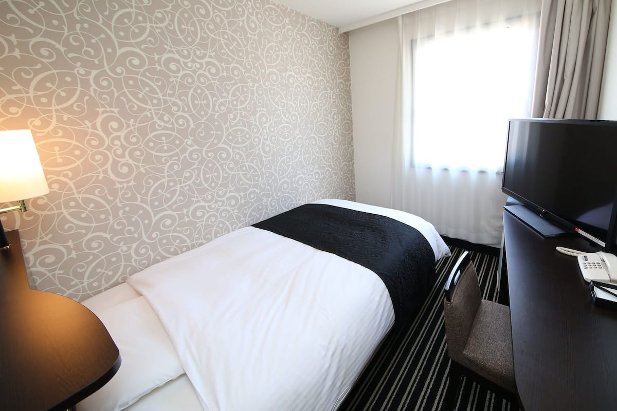 Une chambre d’hôtel avec un lit, un bureau équipé d’une télévision, d’un téléphone et d’une lampe.