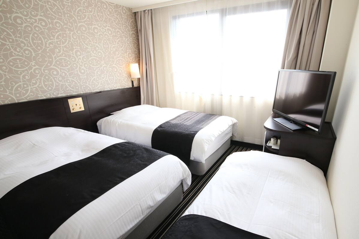 Ein Hotelzimmer mit zwei Betten, einem Fernseher und einem Fenster mit Vorhängen.