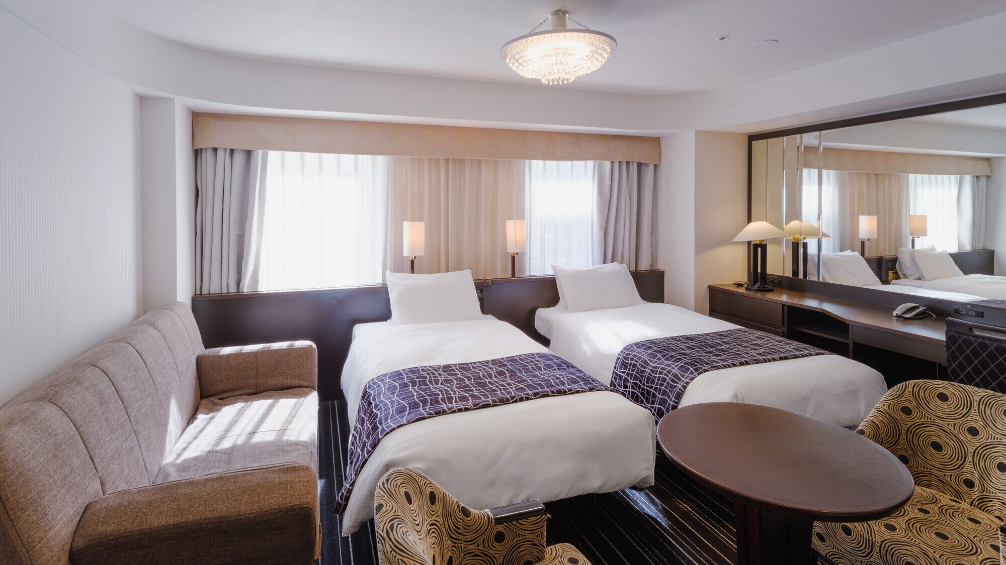 Ein Hotelzimmer mit zwei Betten, einem Sofa, einem kleinen Tisch und einem großen Spiegel.