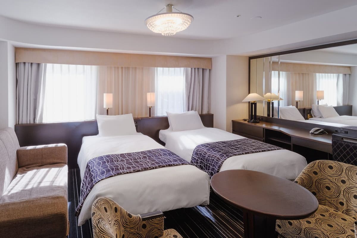 Habitación de hotel con dos camas, un sofá, una mesita pequeña y un espejo grande.