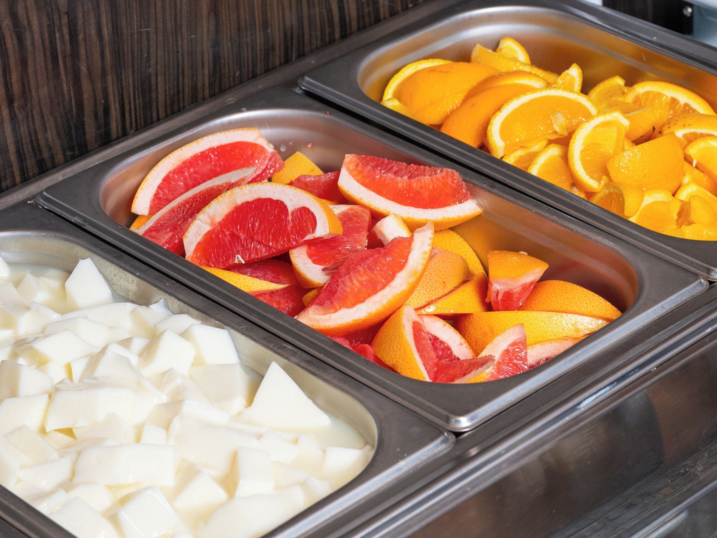 Un bufé con diversas frutas y un recipiente con queso en cubos.
