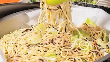A pan of noodles with vegetables and a yellow spatula lifting some noodles.