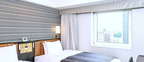 Habitación de hotel con dos camas, un panel de control, una ventana con vista a la ciudad y una lámpara en el techo.