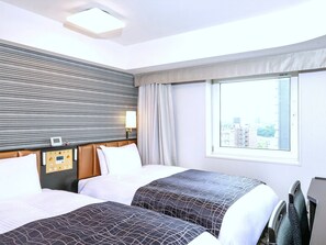 A hotel room with two beds, a control panel, a window with a city view, and a ceiling light.