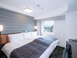 A hotel room with a bed, a desk, a window with a city view, and a patterned headboard.