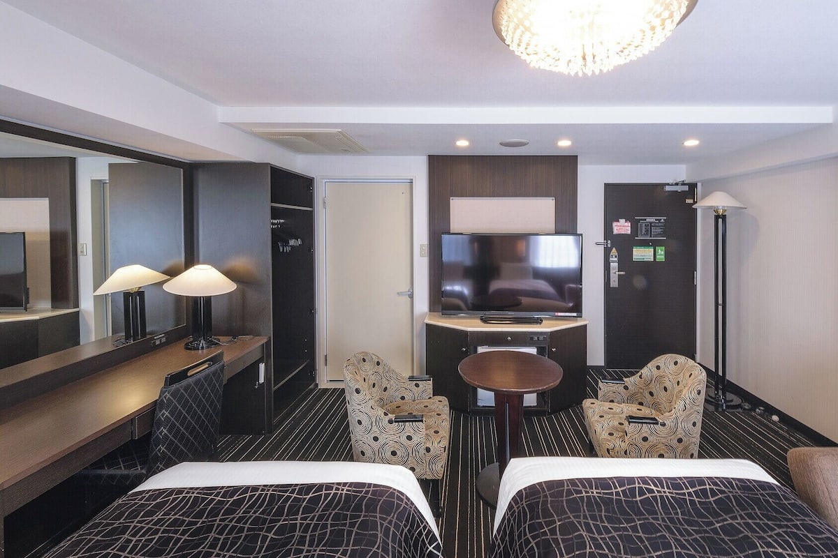 Ett hotellrum med en TV, två sängar, ett skrivbord, en stol och en lampa.