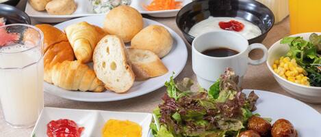 A table with various breakfast items including croissants, hot dogs, and a salad.