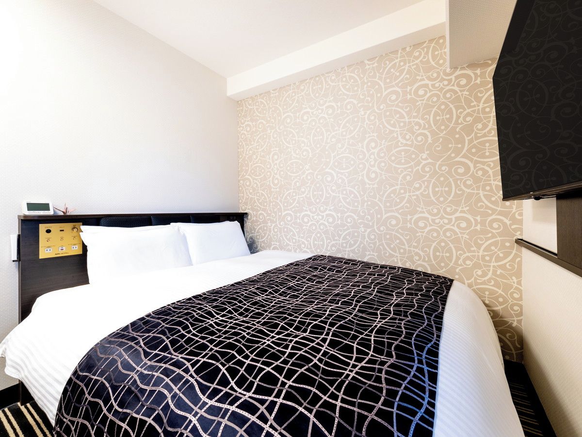 A hotel room with a bed, a control panel, and a patterned wall.