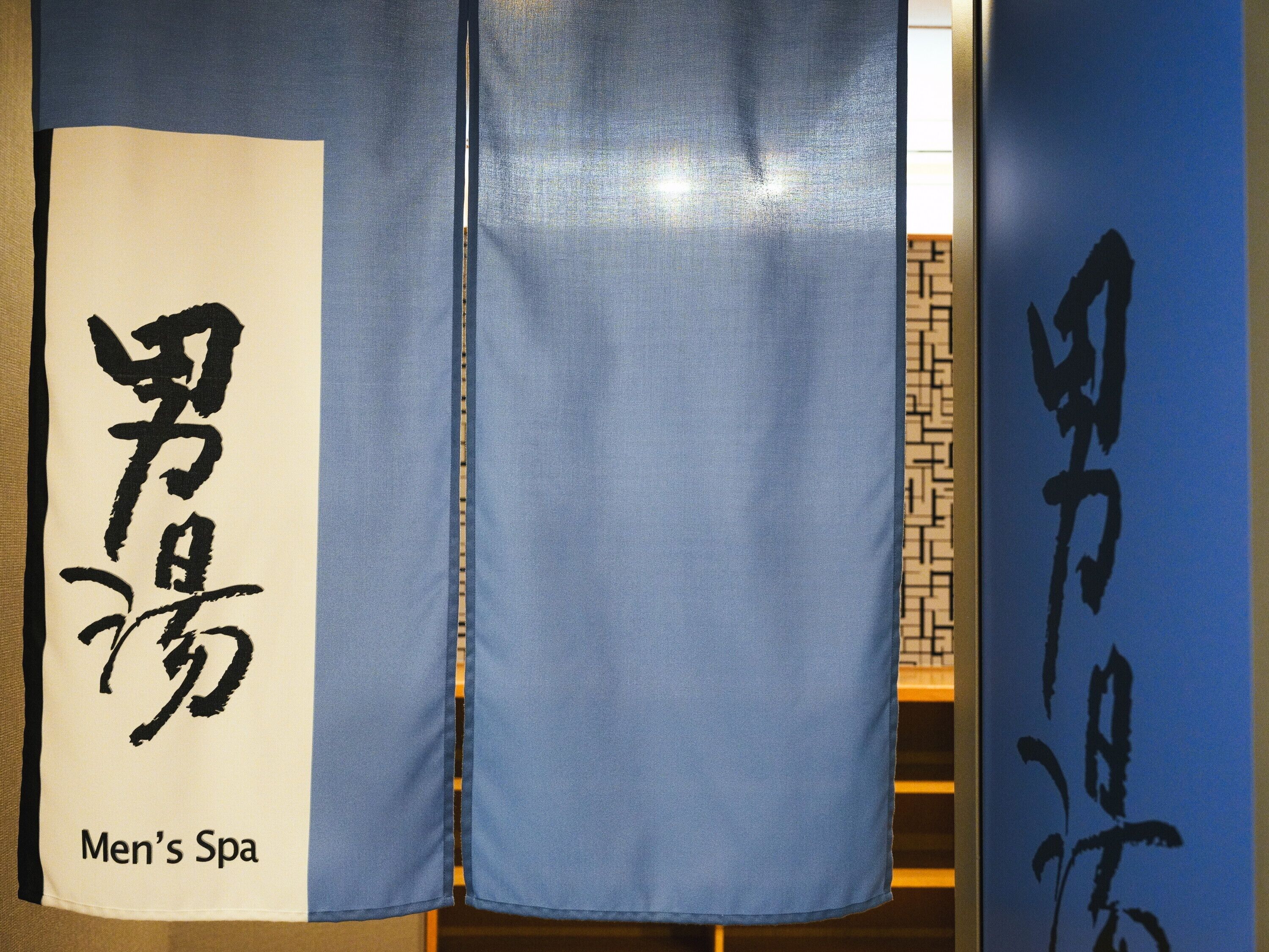 Een kamer met een blauw gordijn en een witte muur met Japanse karakters en de tekst 'Men's Spa'.