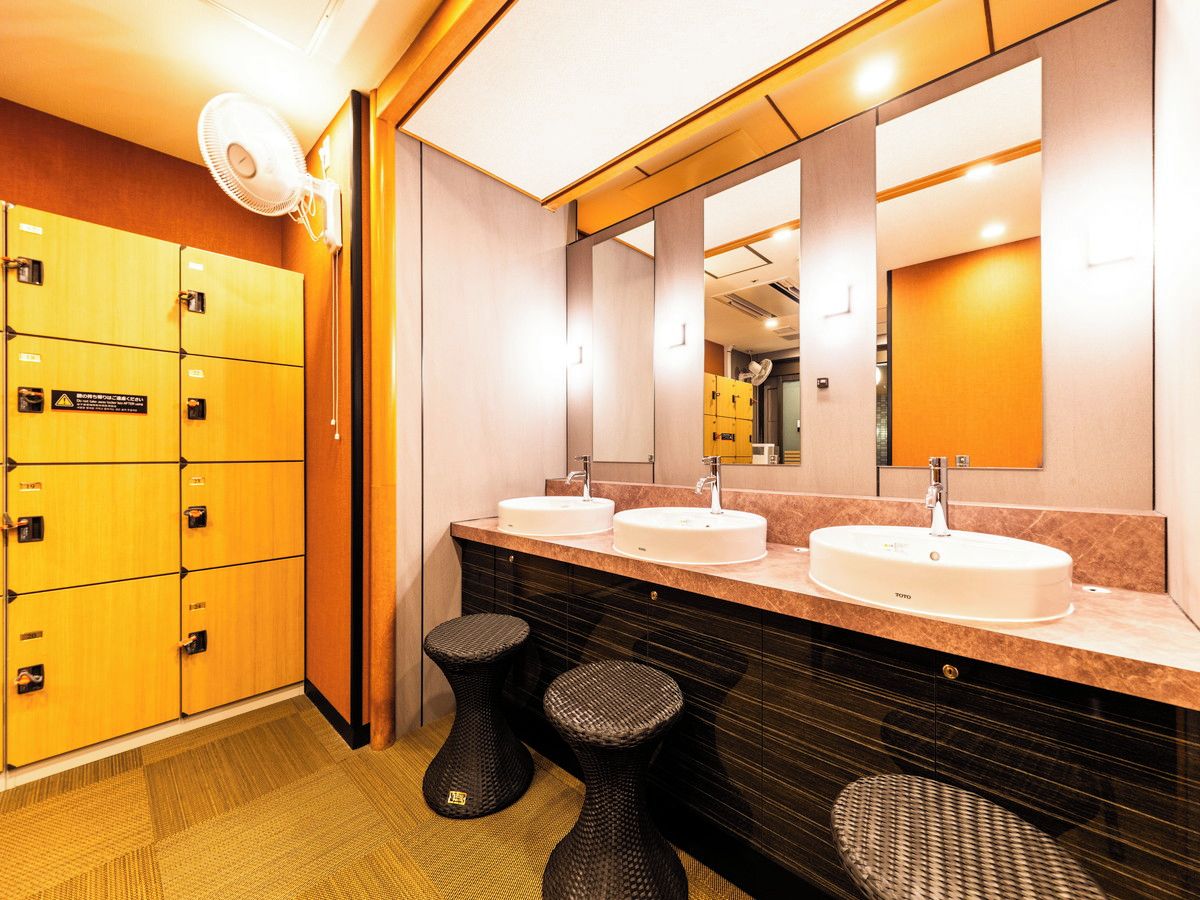 A hotel bathroom with three sinks, a large mirror, and a row of lockers.