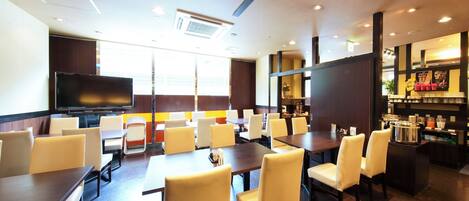 A modern hotel lobby with multiple seating areas, a large flat-screen TV, and a coffee bar.
