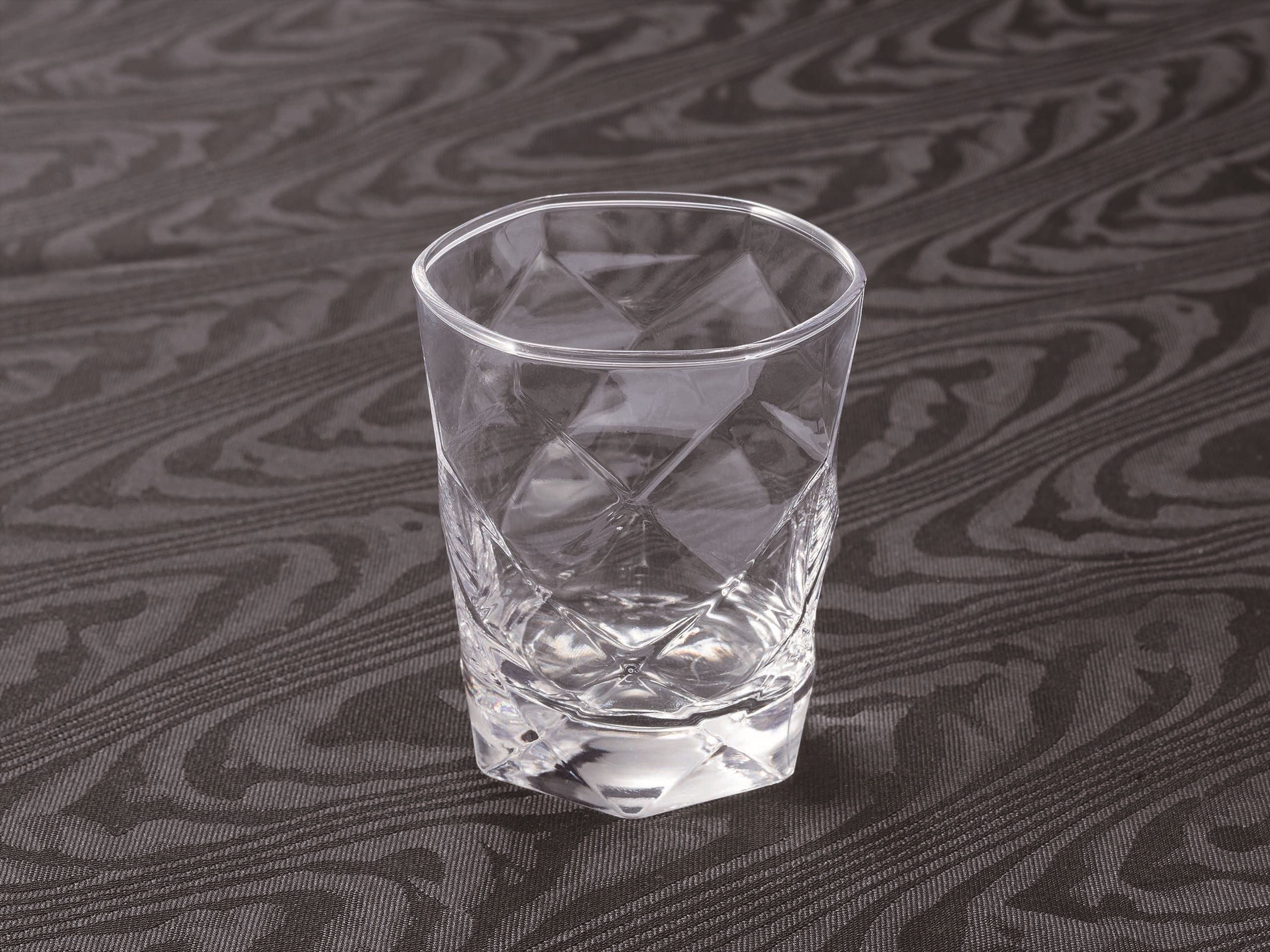 A clear glass tumbler on a textured surface.