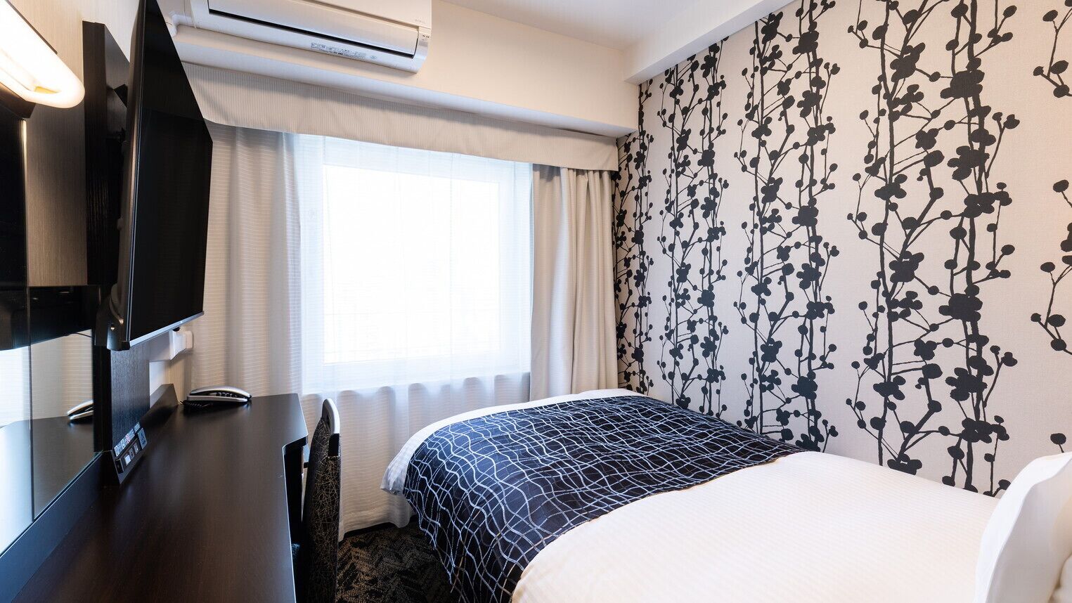 Habitación de hotel con cama, escritorio, televisor y ventana con cortinas.