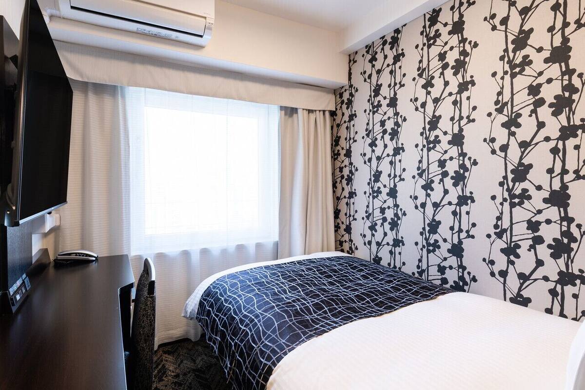 A hotel room with a bed, a desk, a television, and a window with curtains.