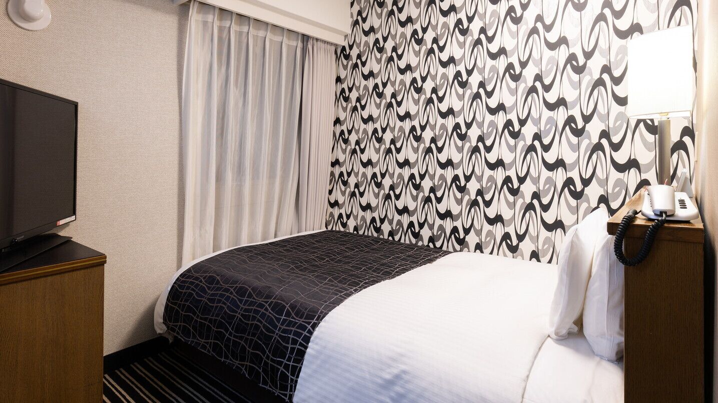 A hotel room with a bed, a television on a wooden cabinet, a telephone, and patterned curtains.