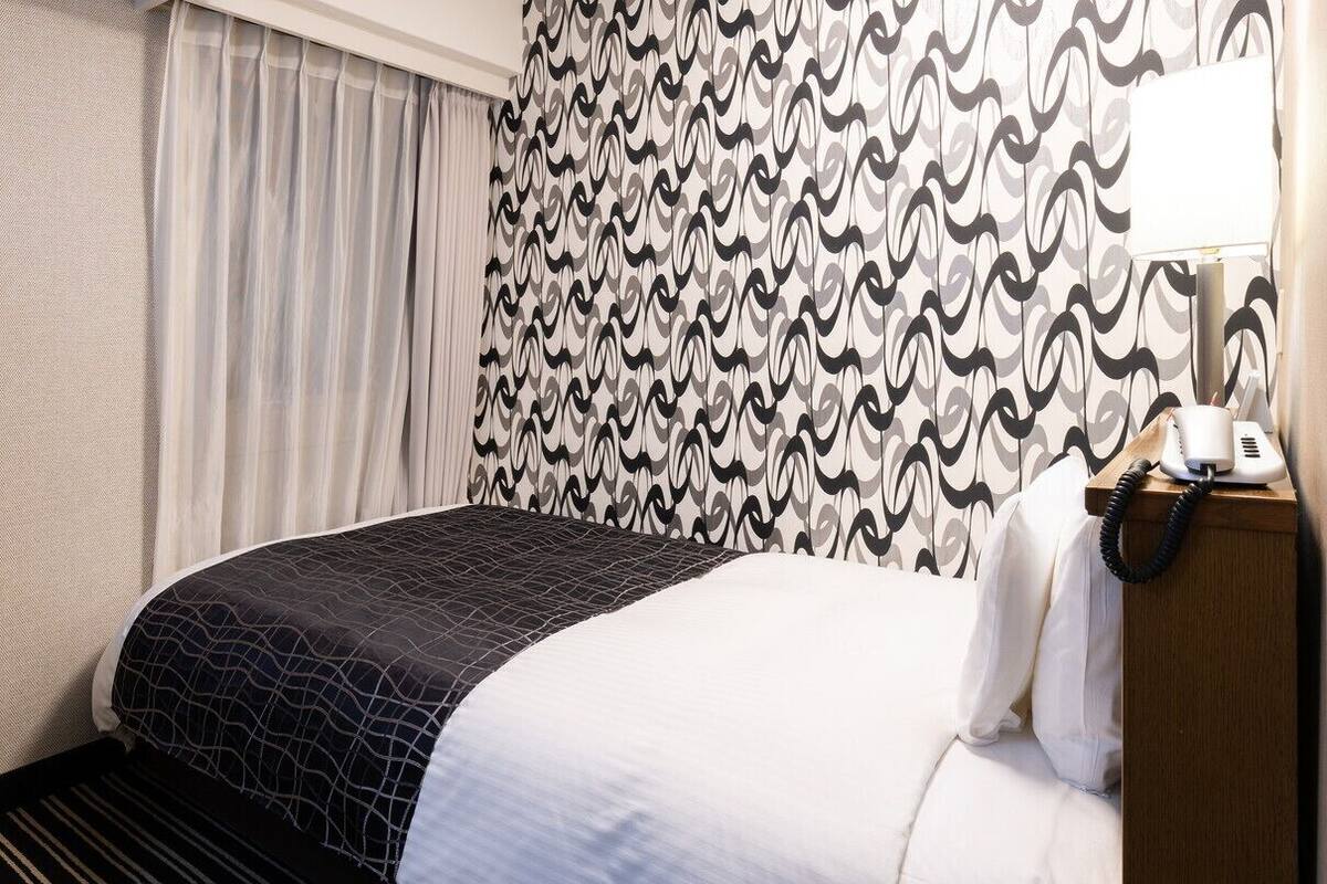 A hotel room with a bed, a television on a wooden cabinet, a telephone, and patterned curtains.