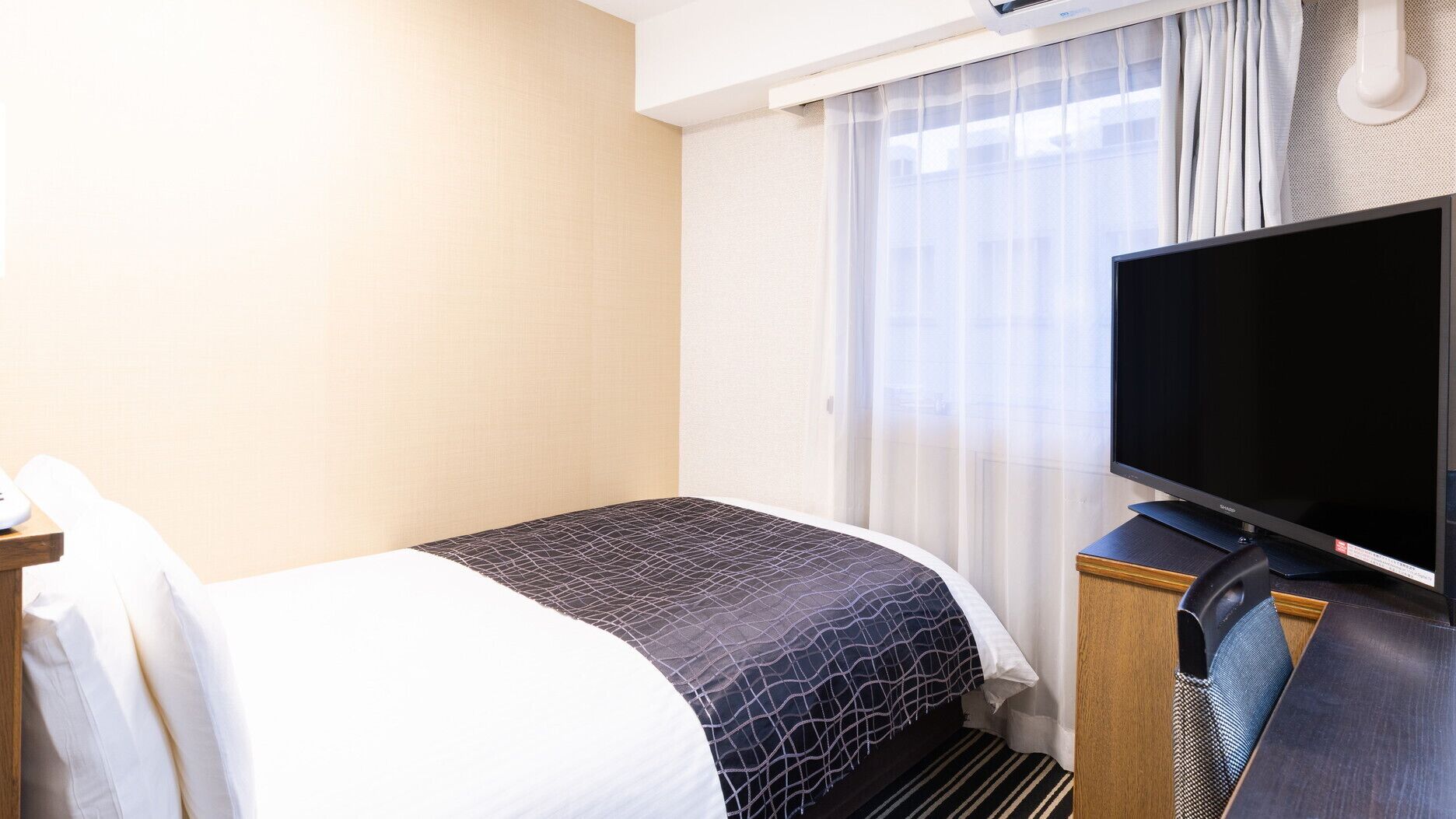 A hotel room with a bed, a television, and a window with curtains.