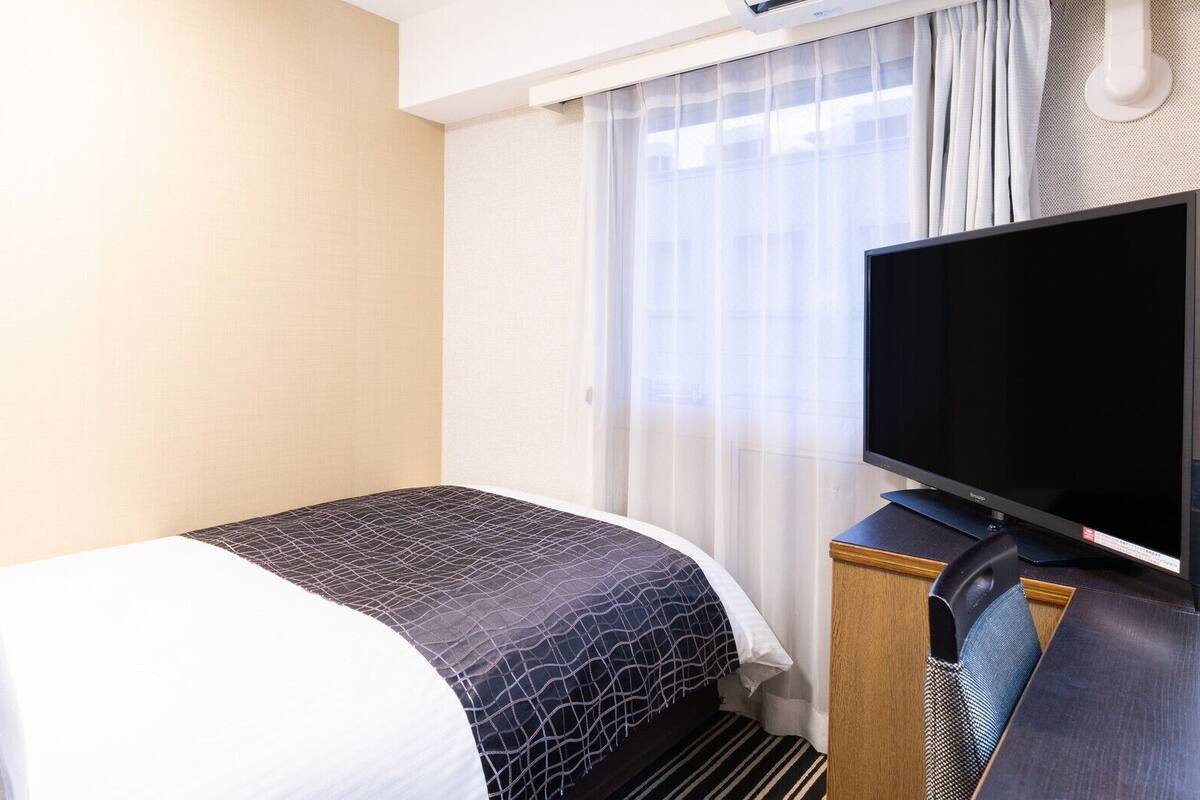 A hotel room with a bed, a television, and a window with curtains.