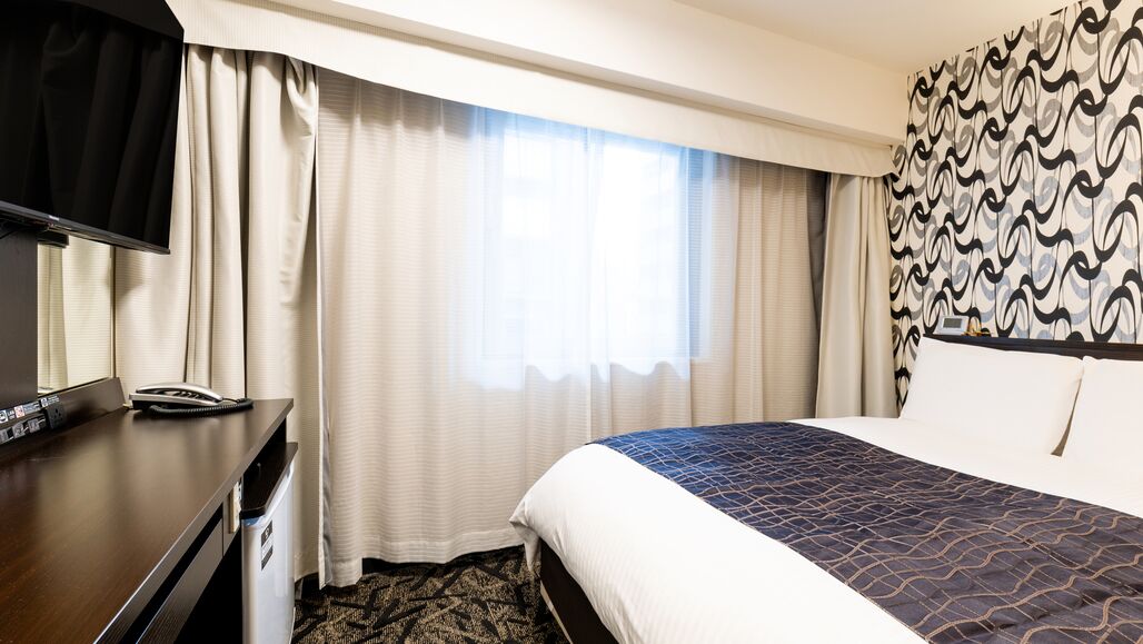 Een hotelkamer met een bed, een bureau met telefoon, een televisie en gordijnen.