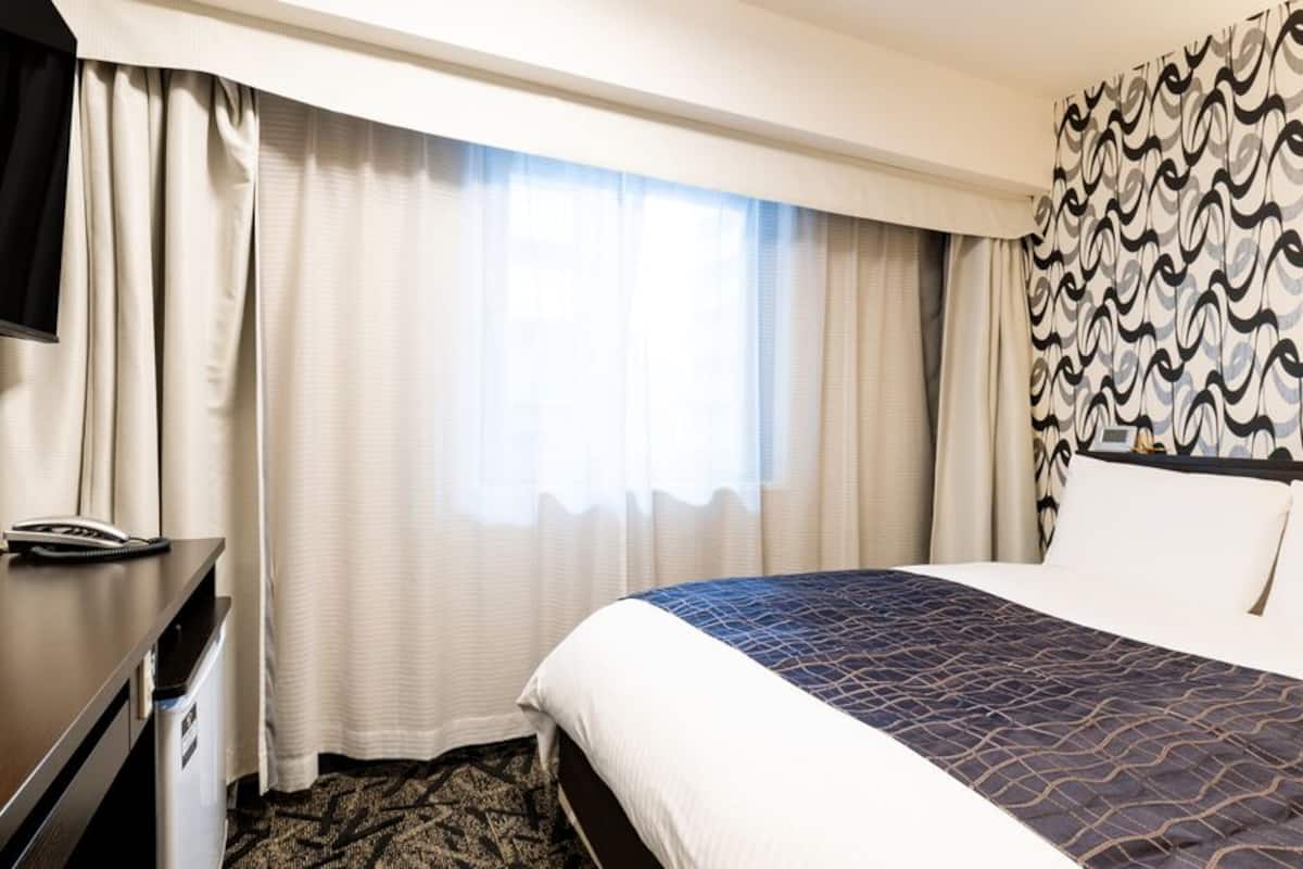 A hotel room with a bed, a desk with a telephone, a television, and curtains.